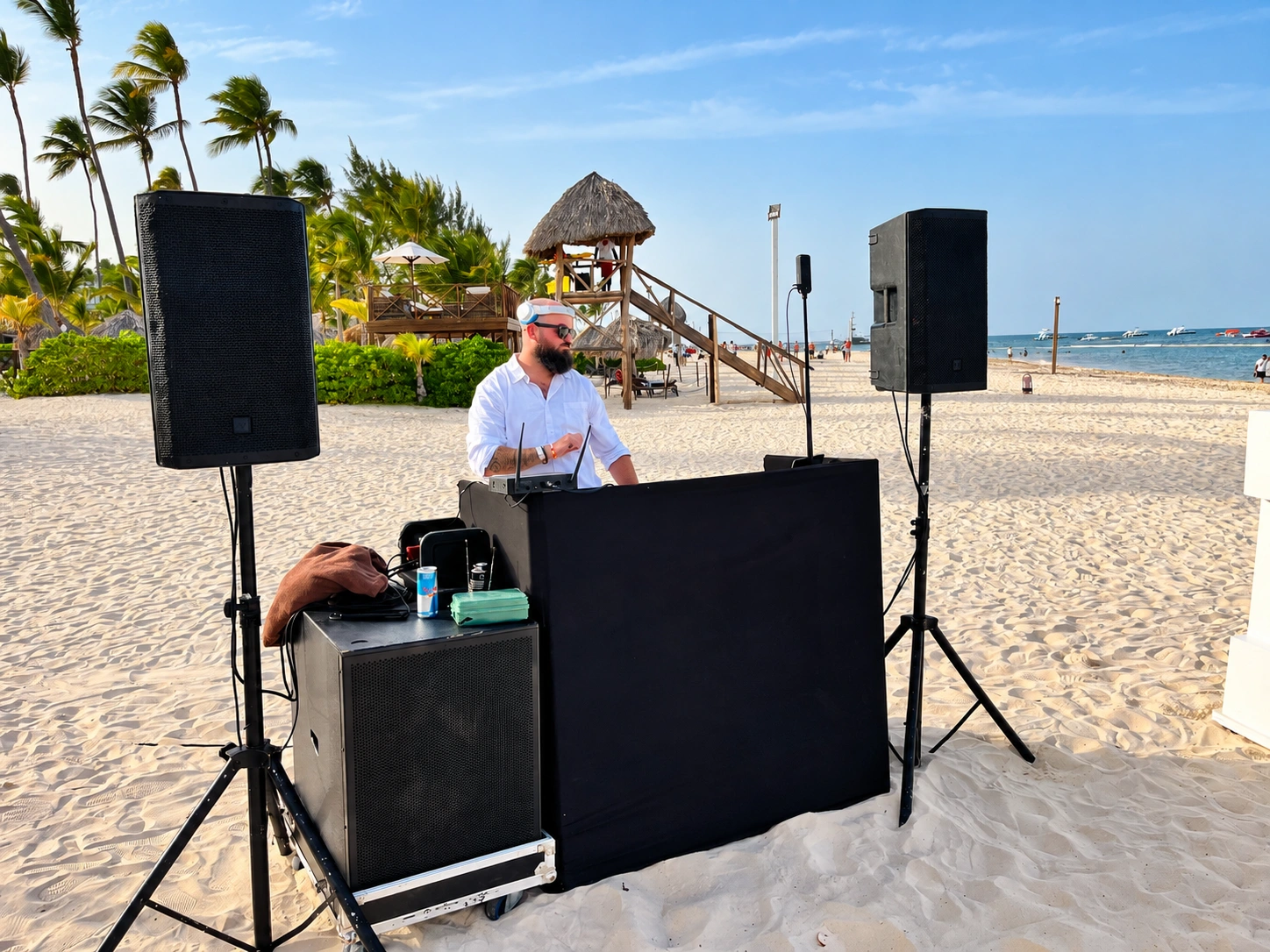 Kyle in a white shirt and headphones performing behind the DJ booth on the beach